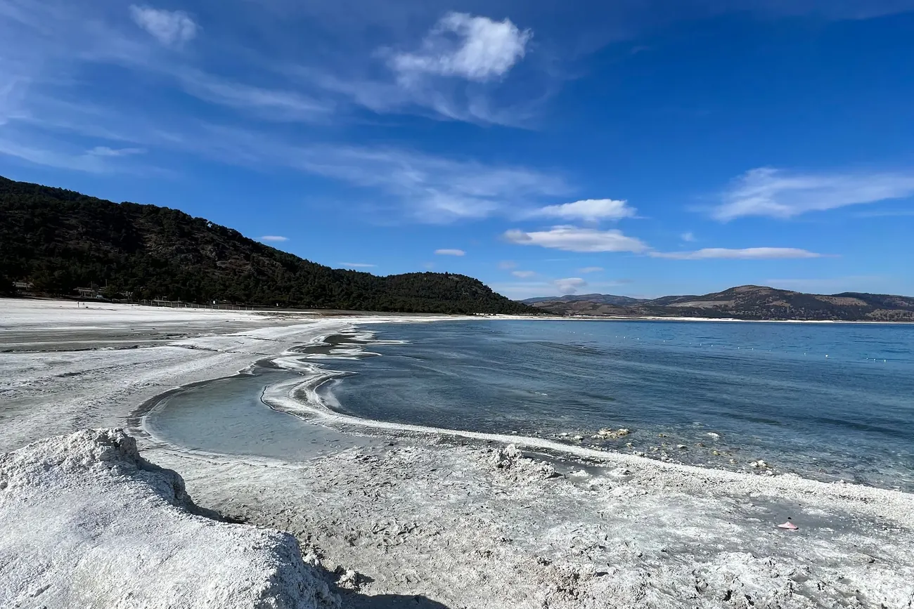 White mineral shoreline of Lake Salda in Burdur meeting clear blue water under a wide sky